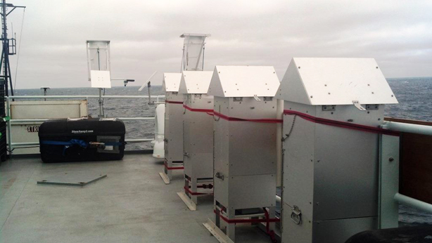 The four aerosol samplers can be seen in the foreground. The sampling filters are protected from sea spray and rain by the roof-like shrouds that give the samplers the appearance of birdhouses. The rain samplers are mounted in the background.