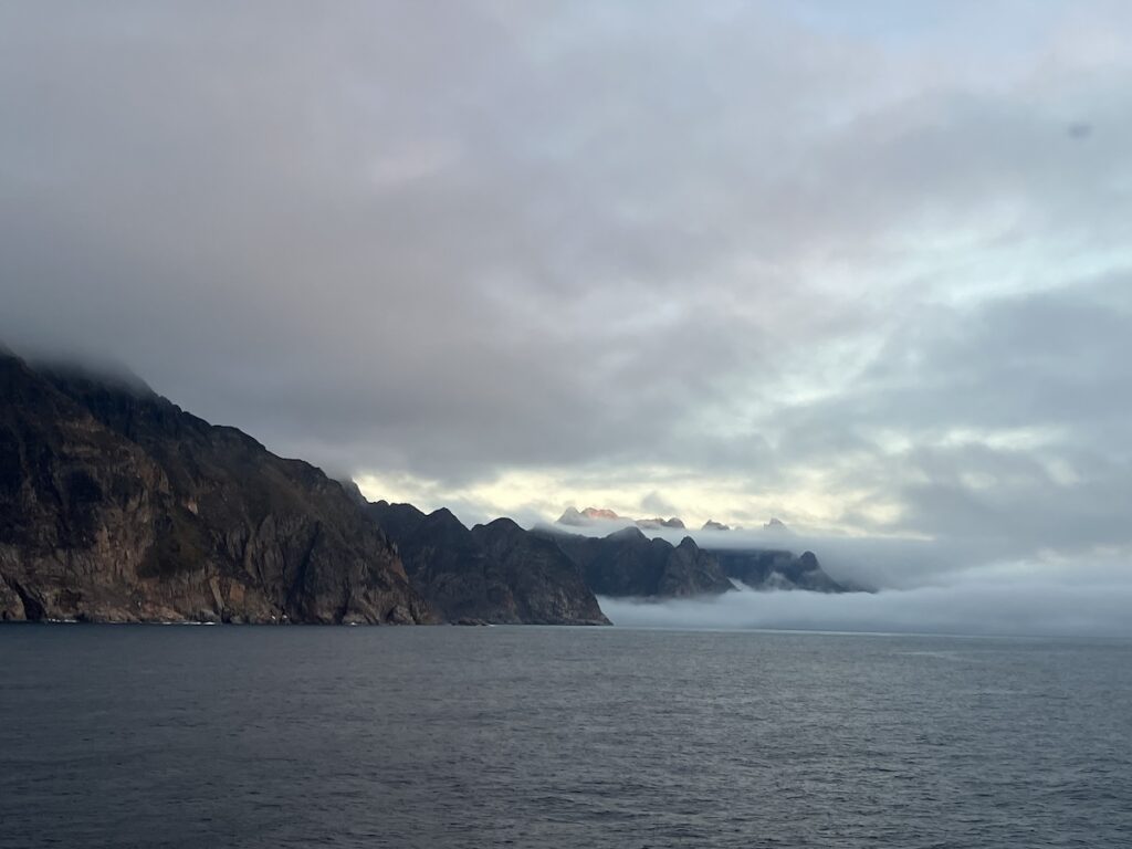 Mountains, surrounded by clouds, poke out of the ocean. 